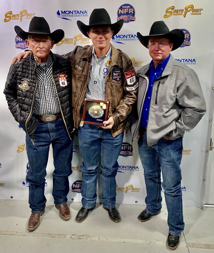 Three men in cowboy hats and Western wear pose with an award at the NFR and Montana Silversmith backdrop