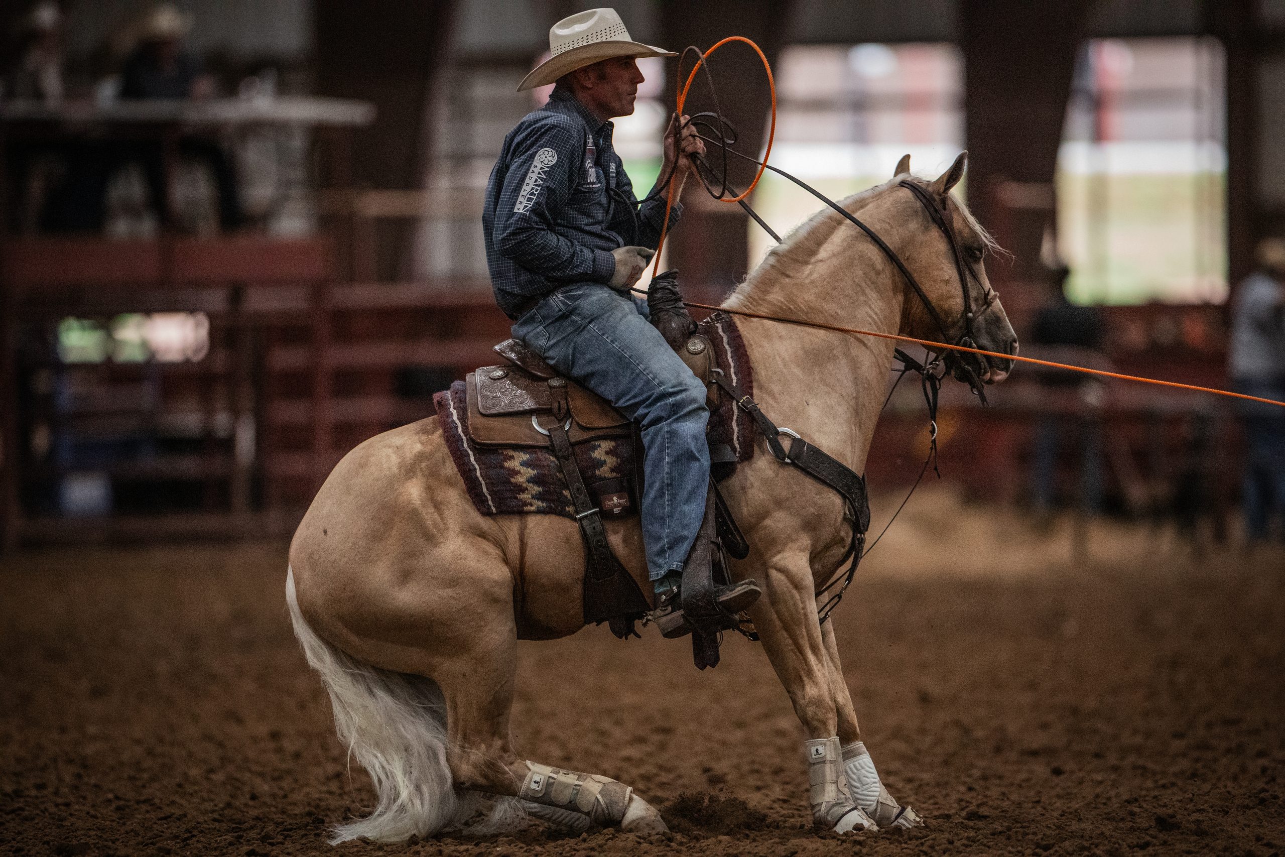 Rodeo competitor on horseback holding a lasso while riding in a dirt arena during a roping event
