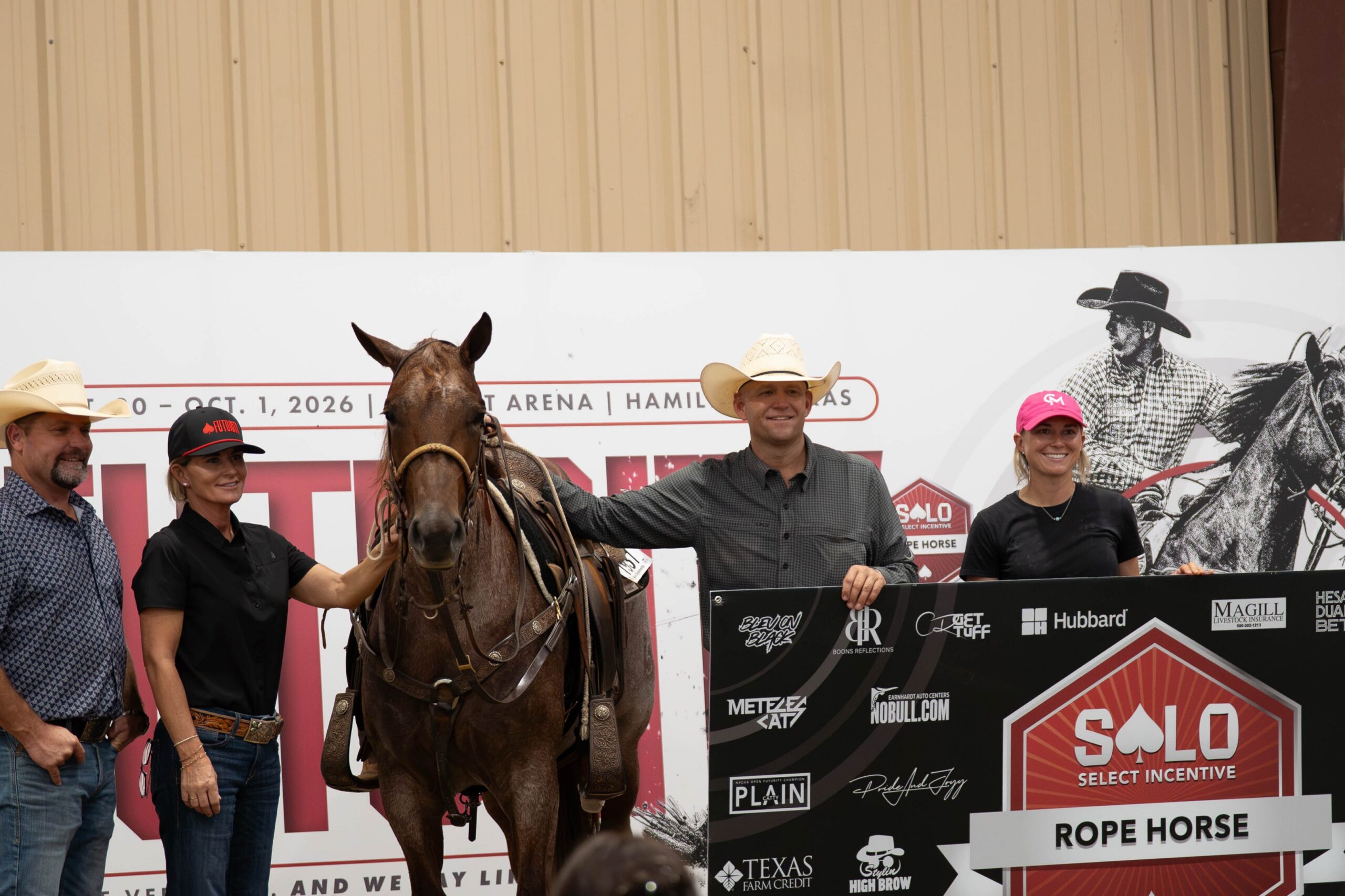 Group of five people with a brown horse holding a banner at a rodeo event in Hamilton, Texas, with sponsor logos visible