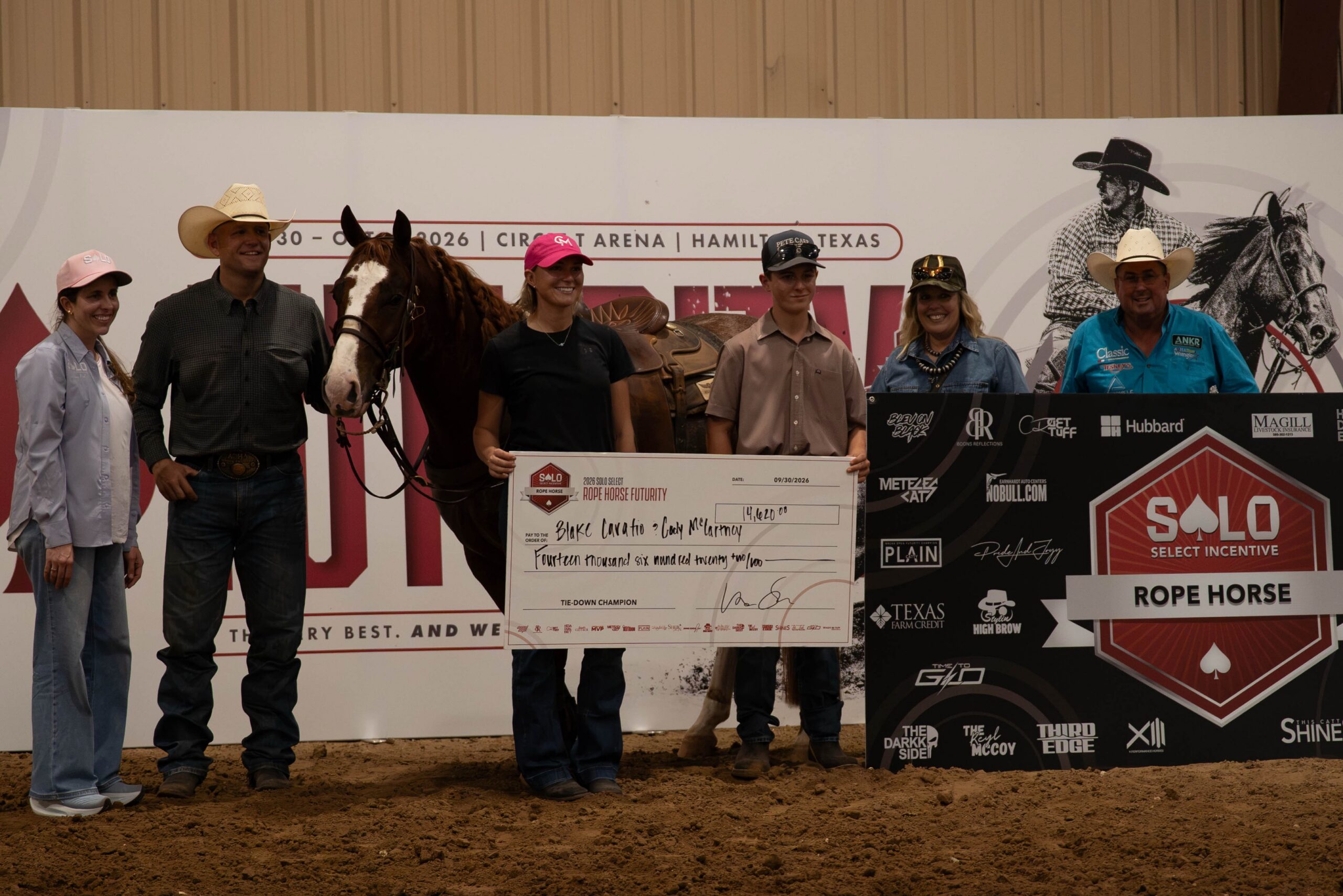 Winners pose with a large check at a rodeo event held at Circuit Arena in Hamilton, Texas, with a horse and sponsors visible in the background