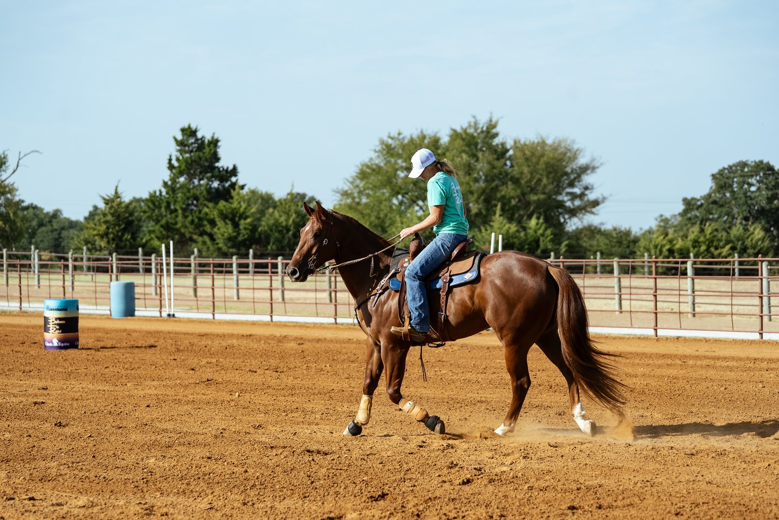 Joy Wargo loping a sorrel horse near a barrel in an outdoor arena