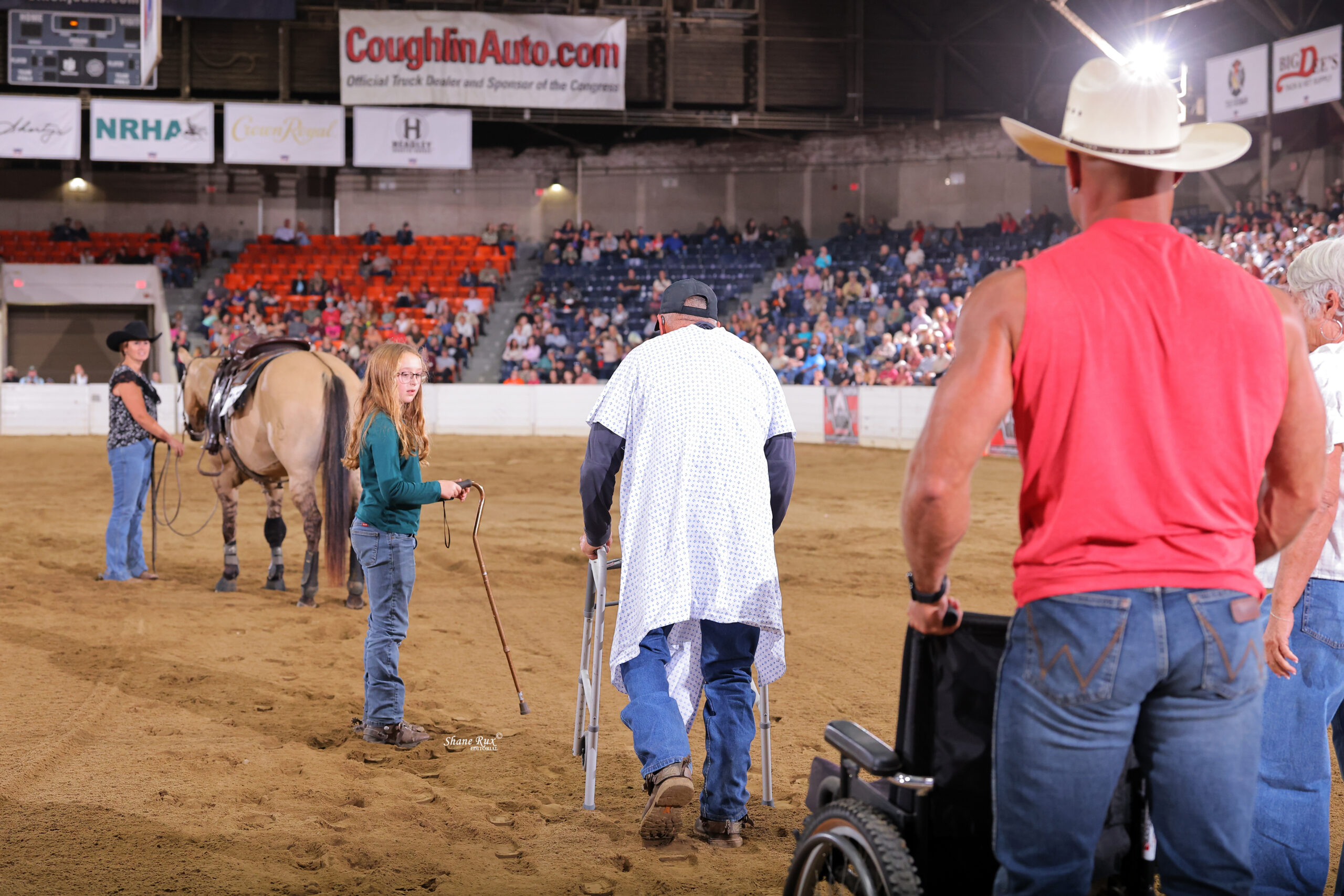 Competitors and handlers work with horses in a dirt arena during a ranch sorting event at an indoor rodeo venue filled with spectators