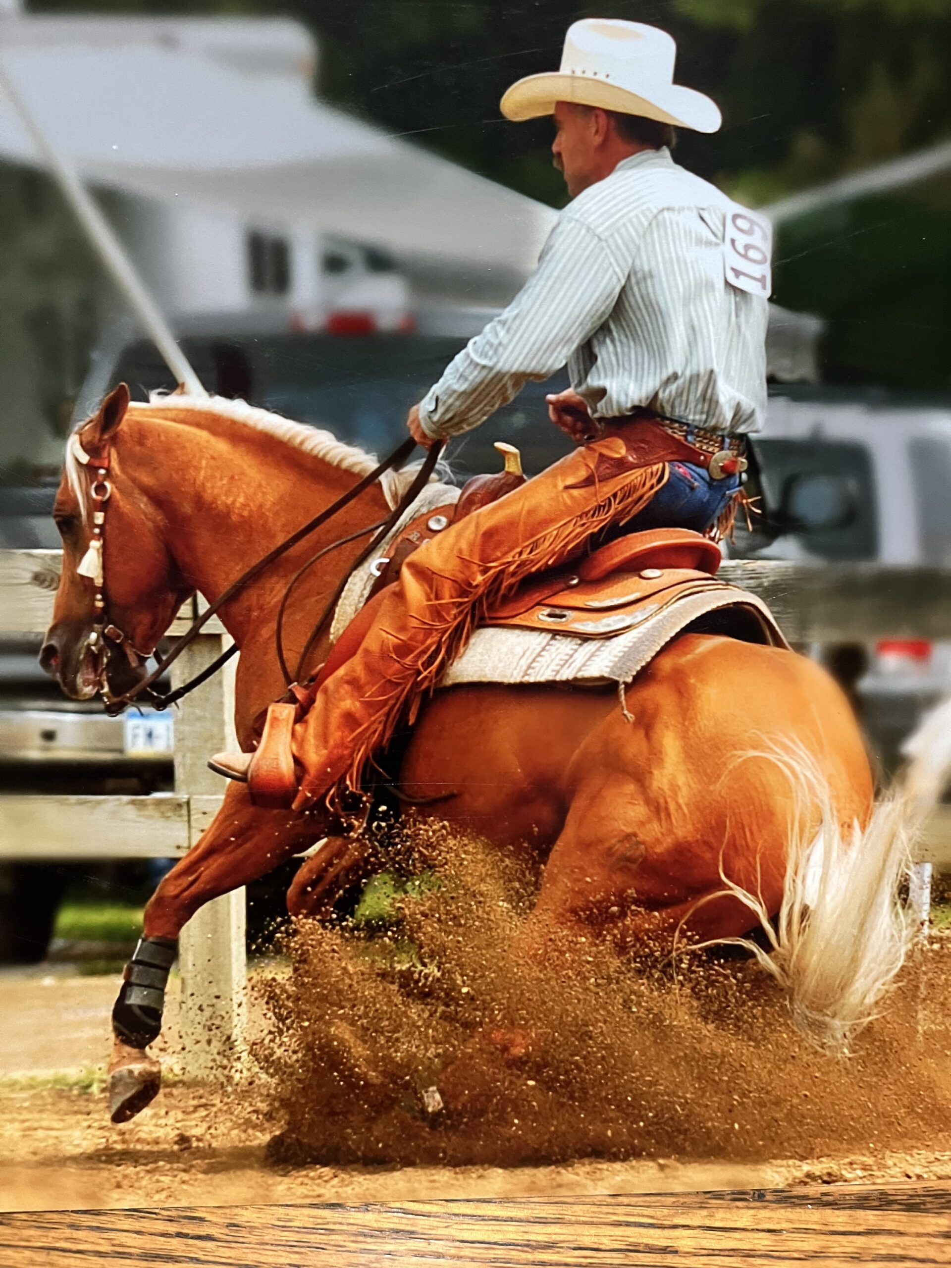 Cowboy in striped shirt and white hat rides a chestnut horse sliding through dirt at a western riding event